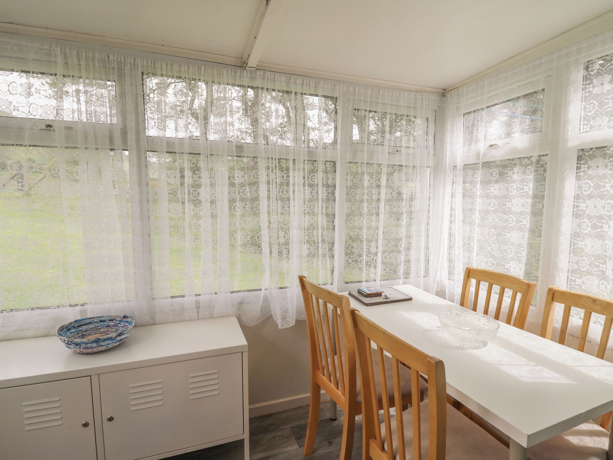 Un comedor con una mesa blanca, sillas de madera y un mueble blanco con un cuenco estampado encima.