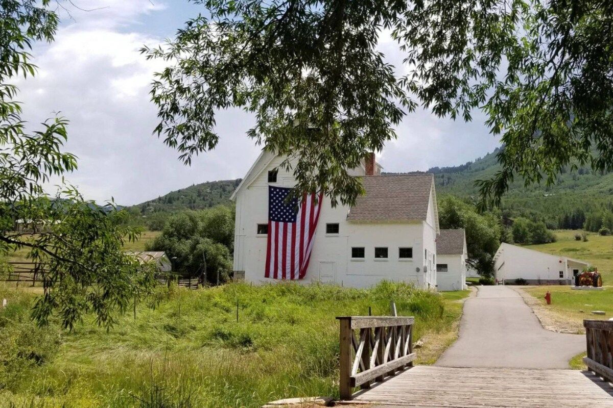 Un bâtiment blanc orné d’un drapeau américain, un sentier en bois et un paysage rural.