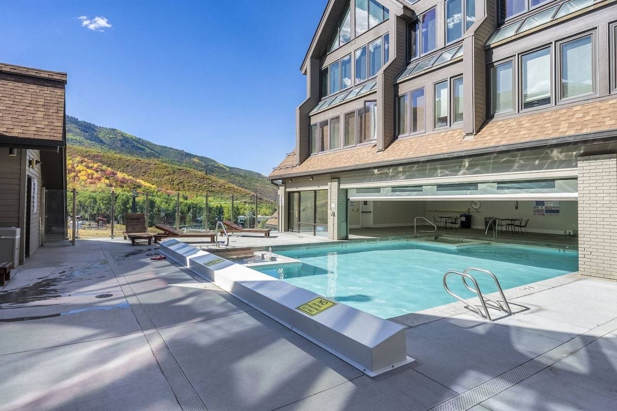 A swimming pool area with a clear view of the pool, a covered seating area, and a mountain backdrop.