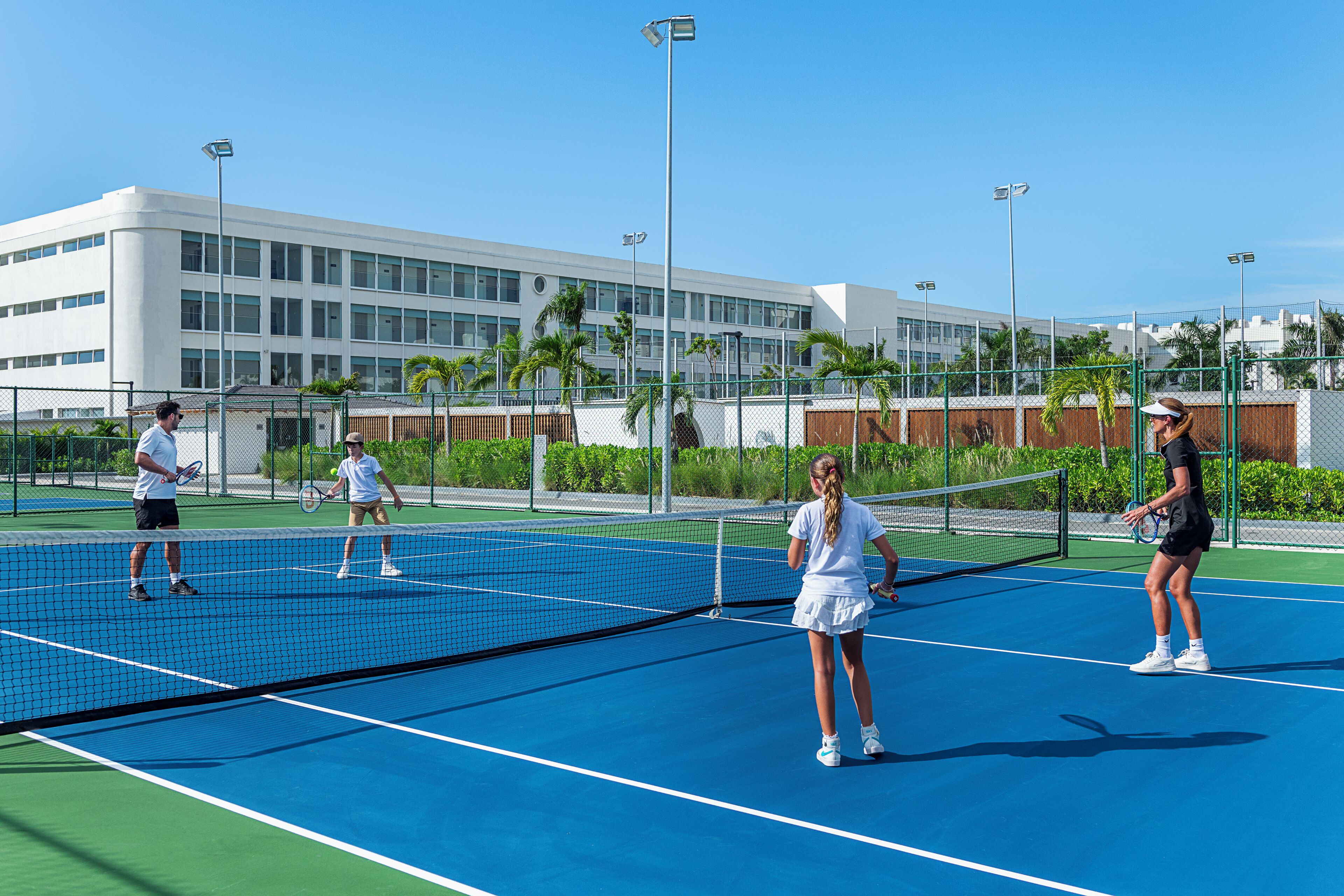 Un court de tennis avec un filet, entouré d’une clôture, et un bâtiment en arrière-plan.