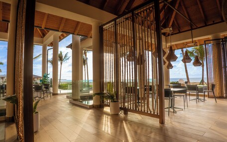 A spacious outdoor area with wooden flooring, seating arrangements, and a view of the beach.
