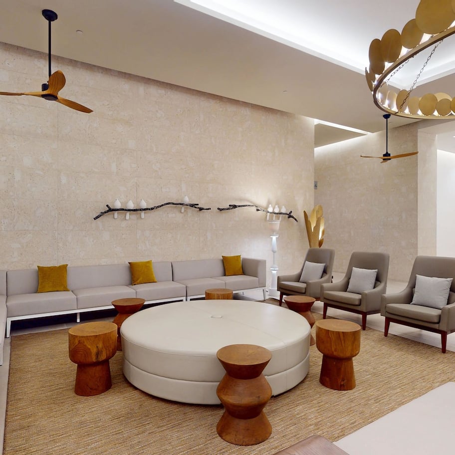 A modern living room with a sectional sofa, armchairs, a round coffee table, wooden side tables, and a ceiling fan.
