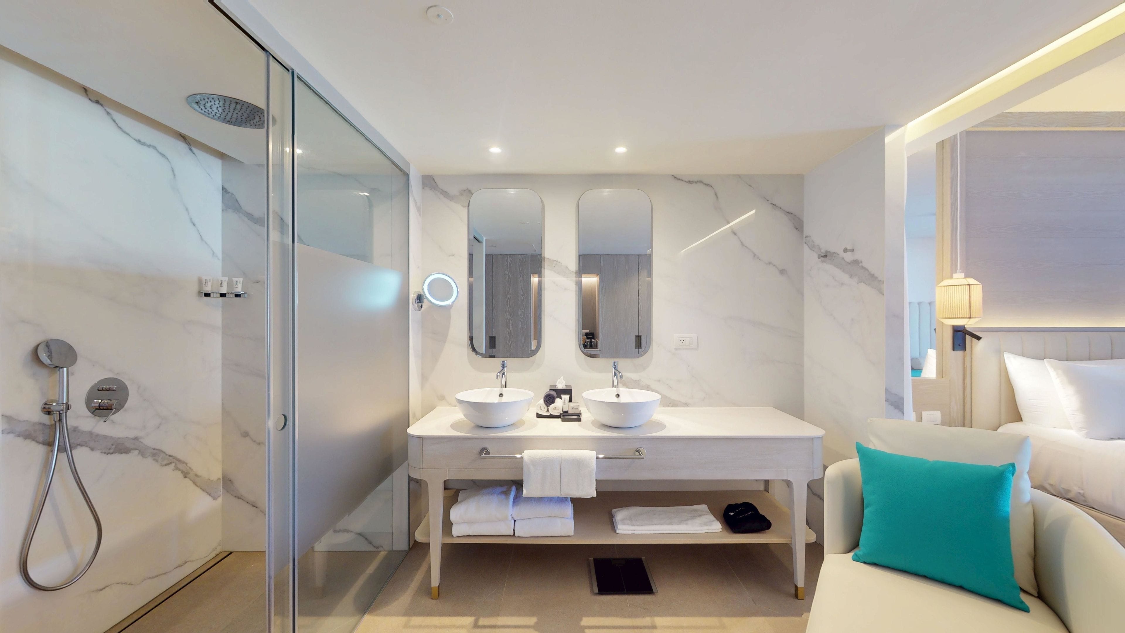 Een moderne badkamer met een douche met glazen wand, twee wasbakken en een badmeubel met een handdoekhouder.