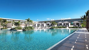 A large outdoor swimming pool with lounge chairs and umbrellas, surrounded by palm trees and a hotel building in the background. - Princess Grand Jamaica Resort - All Inclusive (Green Island)