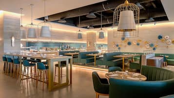 Un interior de restaurante moderno con asientos de bar, cabinas y una cocina al fondo.