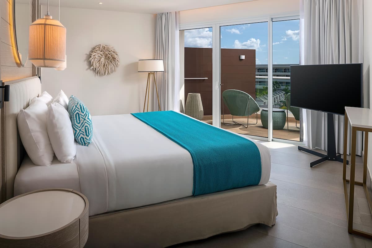 Ein Hotelzimmer mit Bett, Fernseher, einem Balkon mit Stuhl und Blick auf die Stadt.