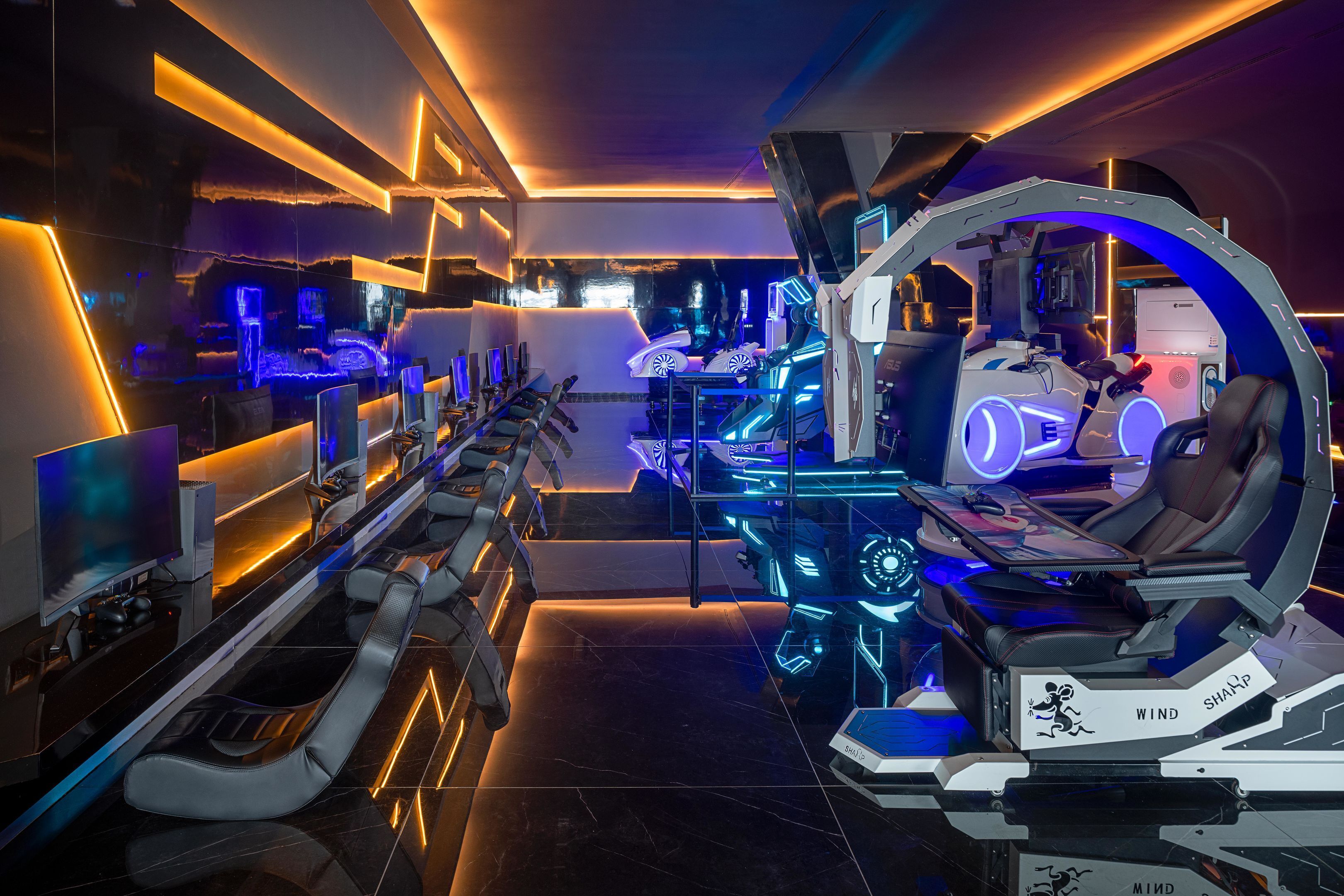 Uma sala de jogos futurista com várias estações de jogo, iluminação neon e uma cadeira gamer grande e curvada.