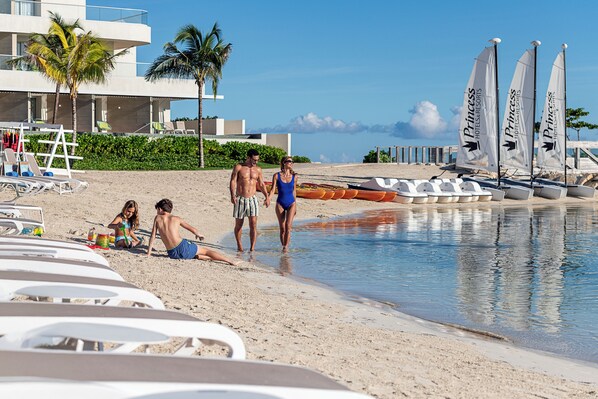 Una playa con sillas de descanso, una piscina y veleros.