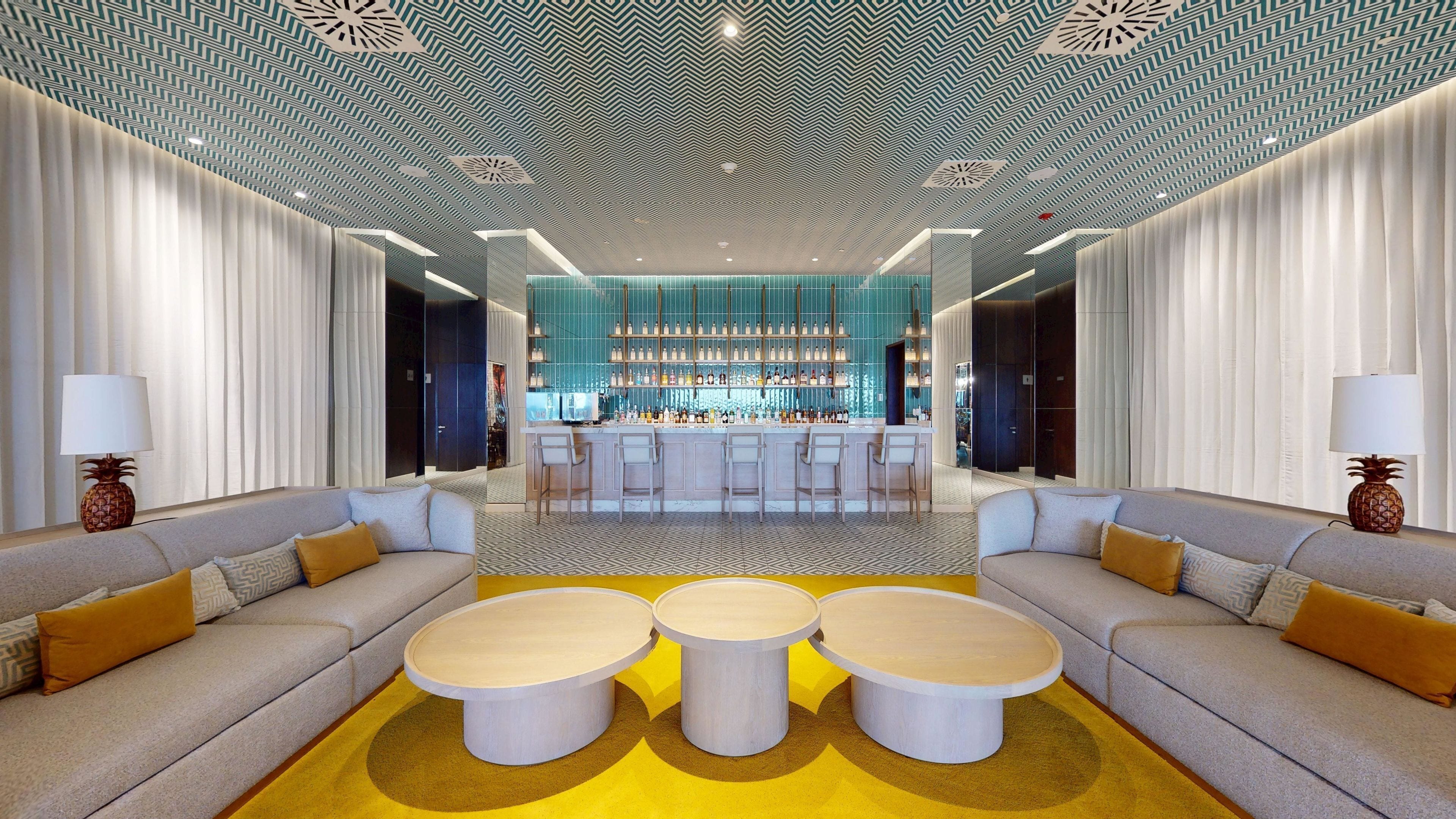 Una hall d'albergo moderna con un bar centrale, divani e un soffitto decorato.