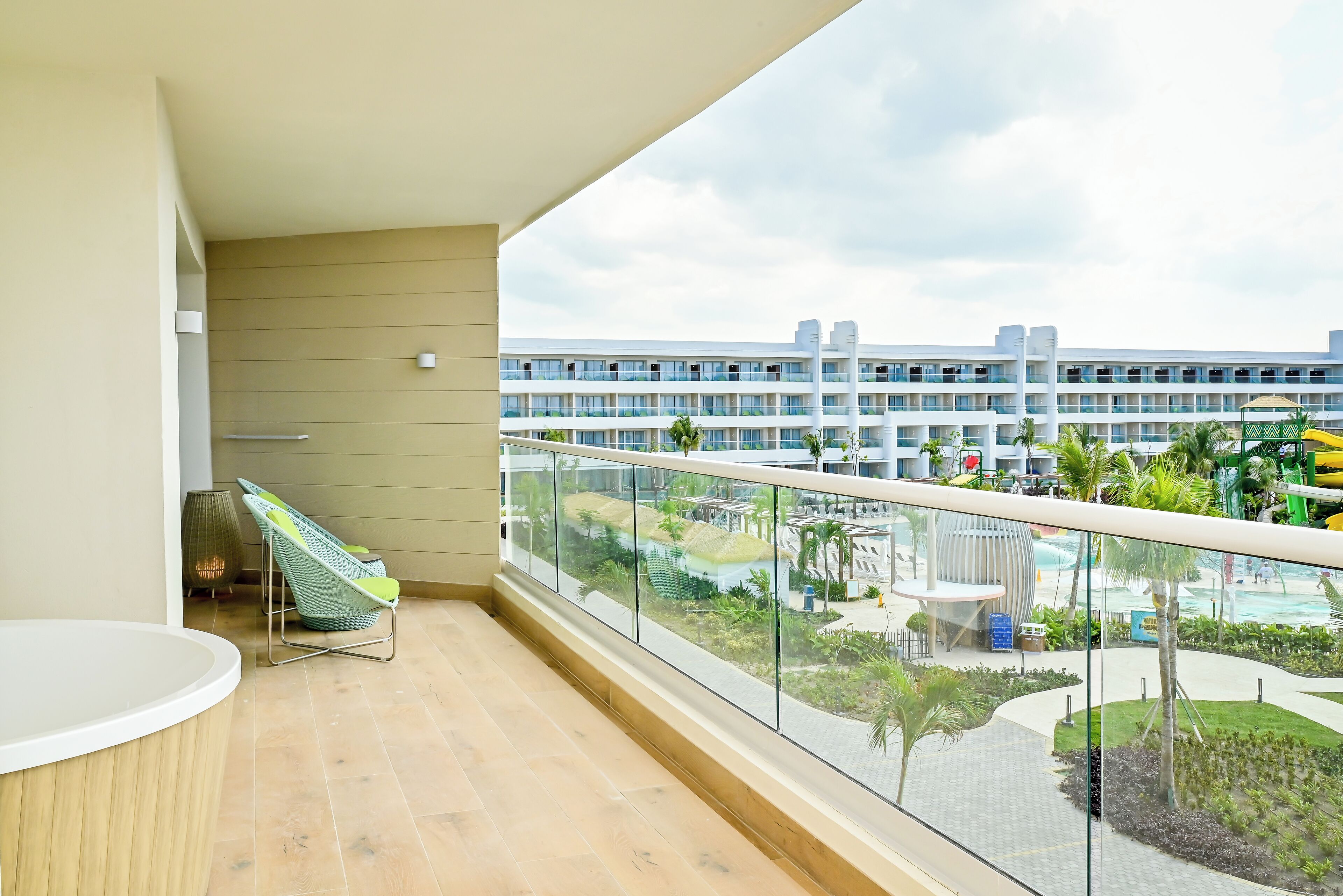Ein Balkon mit Glasgeländer, der auf einen Poolbereich und ein mehrstöckiges Gebäude blickt.