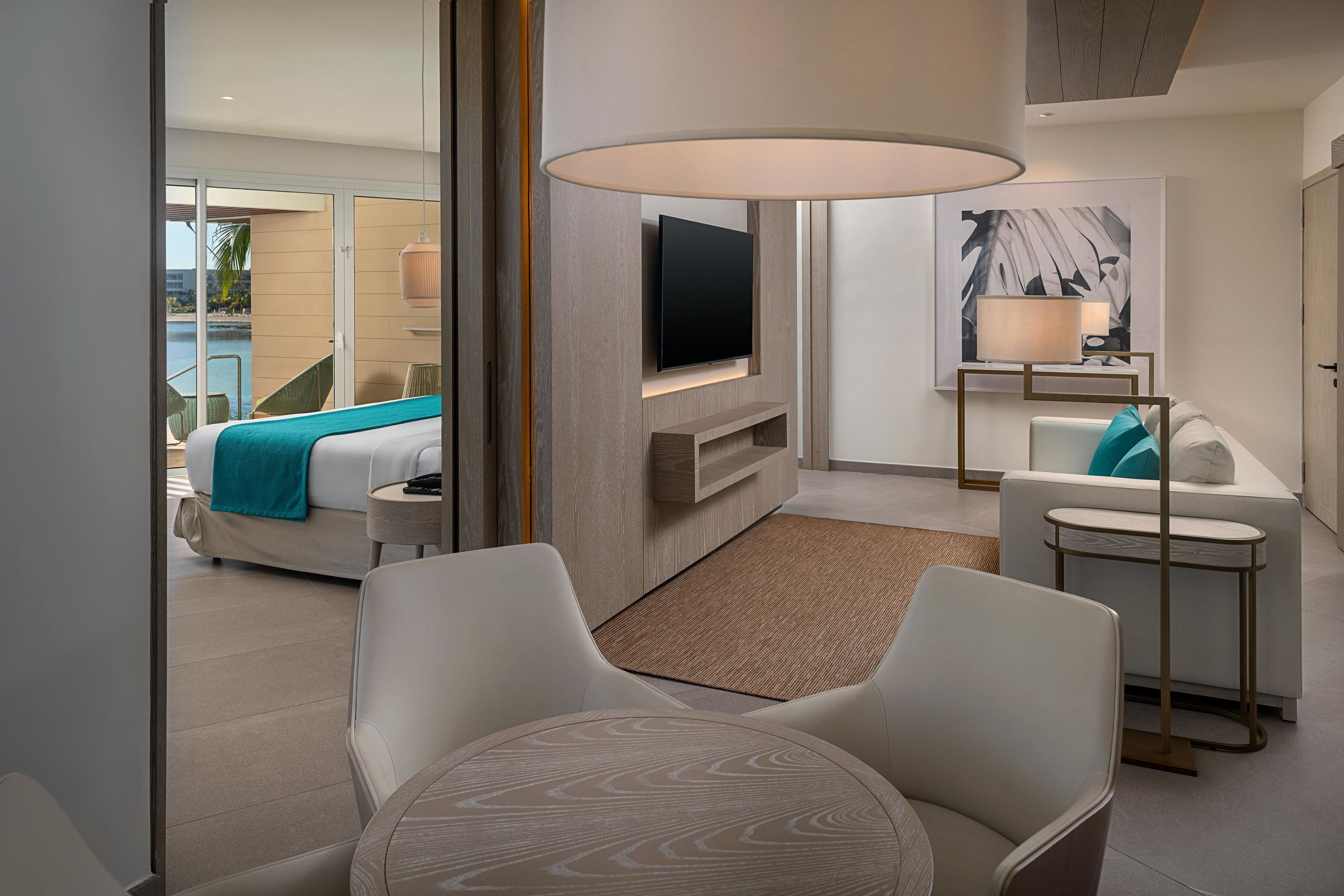Een moderne hotelkamer met een bed, een televisie, een sofa, een tafeltje en uitzicht op het zwembad.
