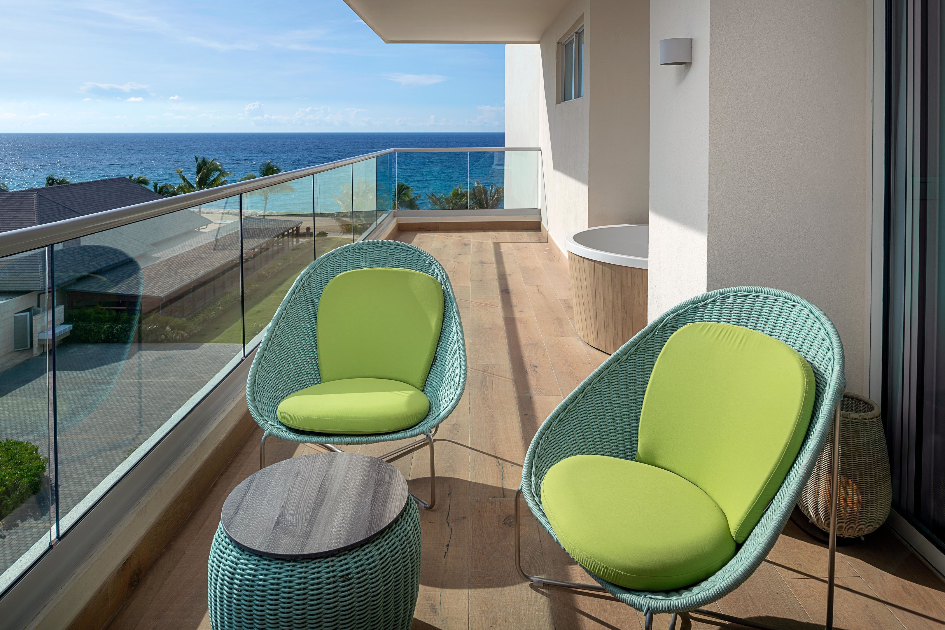 A balcony with wicker chairs and a small table, overlooking a beach and ocean.