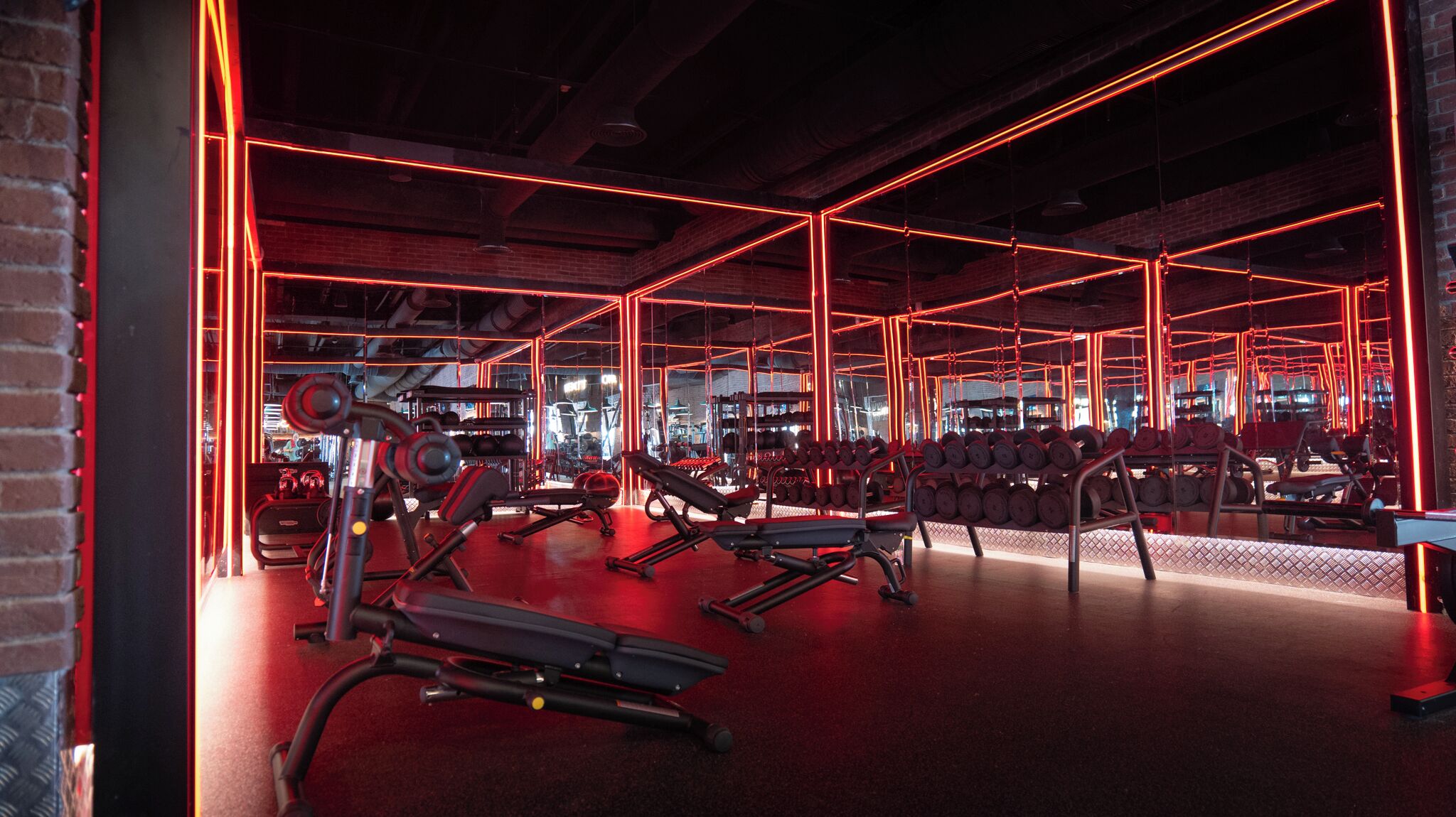 Un gimnasio con iluminación de neón roja, equipamiento de ejercicio y una pared de ladrillo.