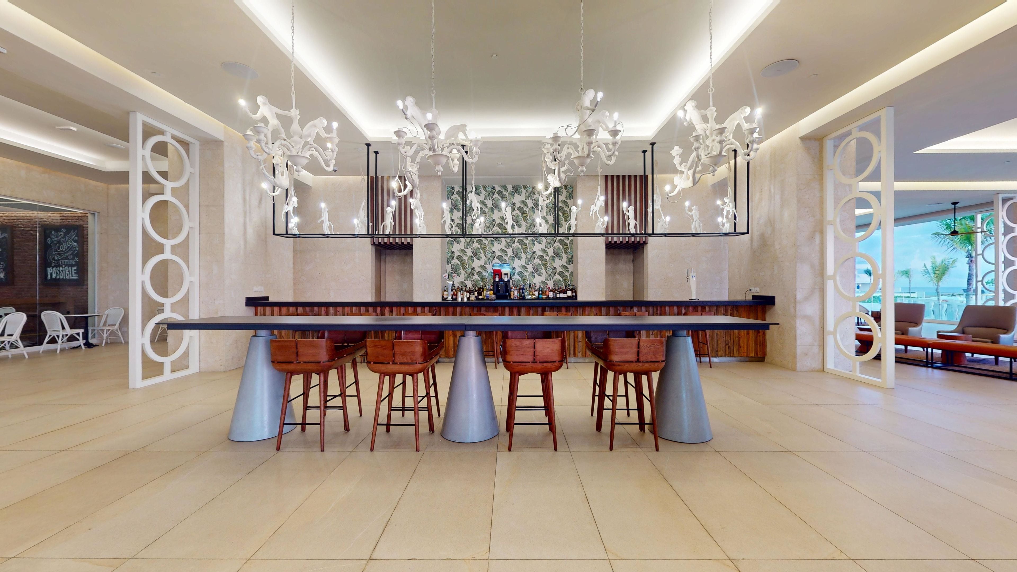 A modern bar area with a long counter, multiple stools, and a decorative chandelier.