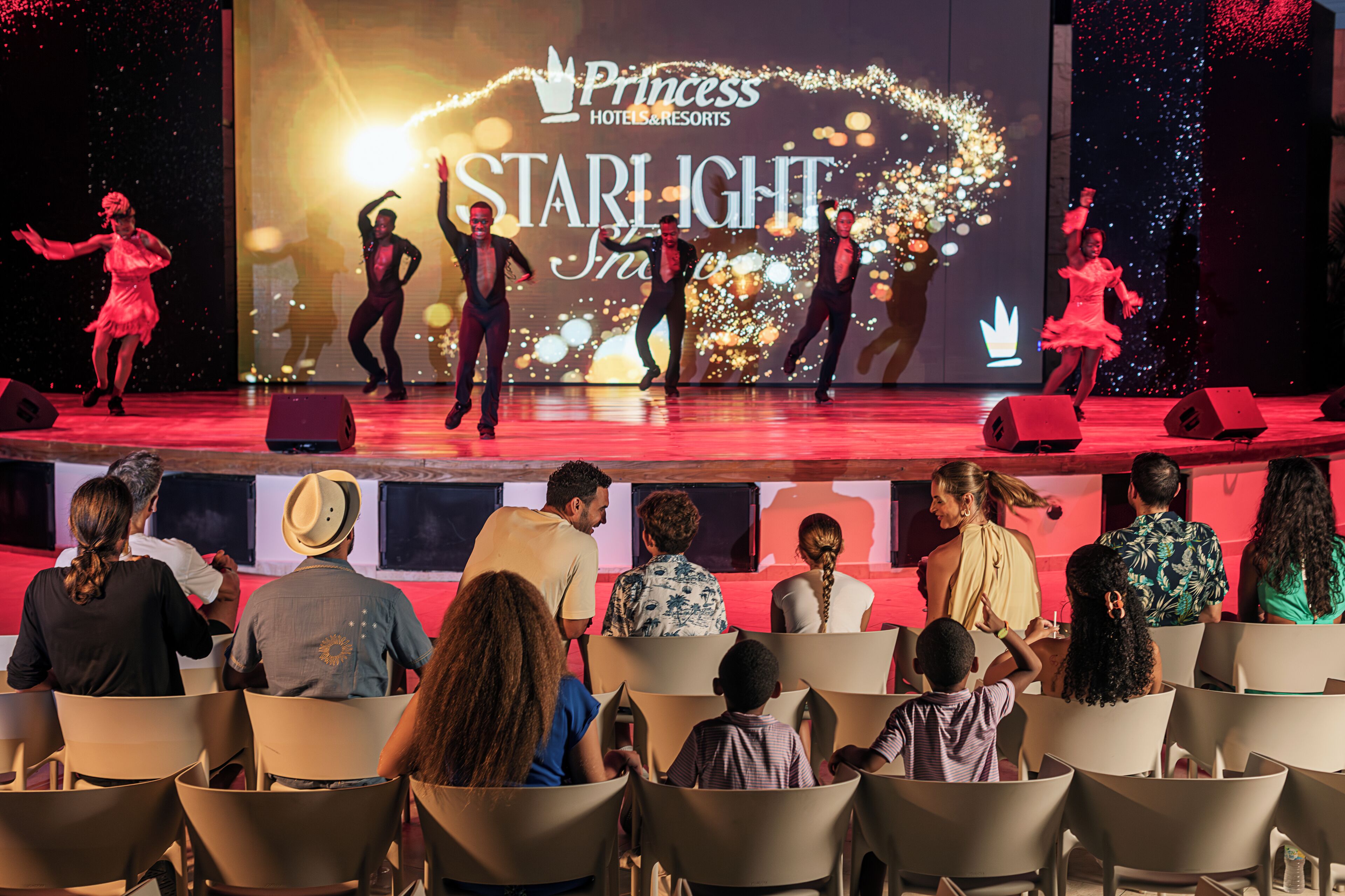 A stage with dancers performing, an audience seated in chairs, and a large screen displaying 'Princess Hotels & Resorts' and 'Starlight'.