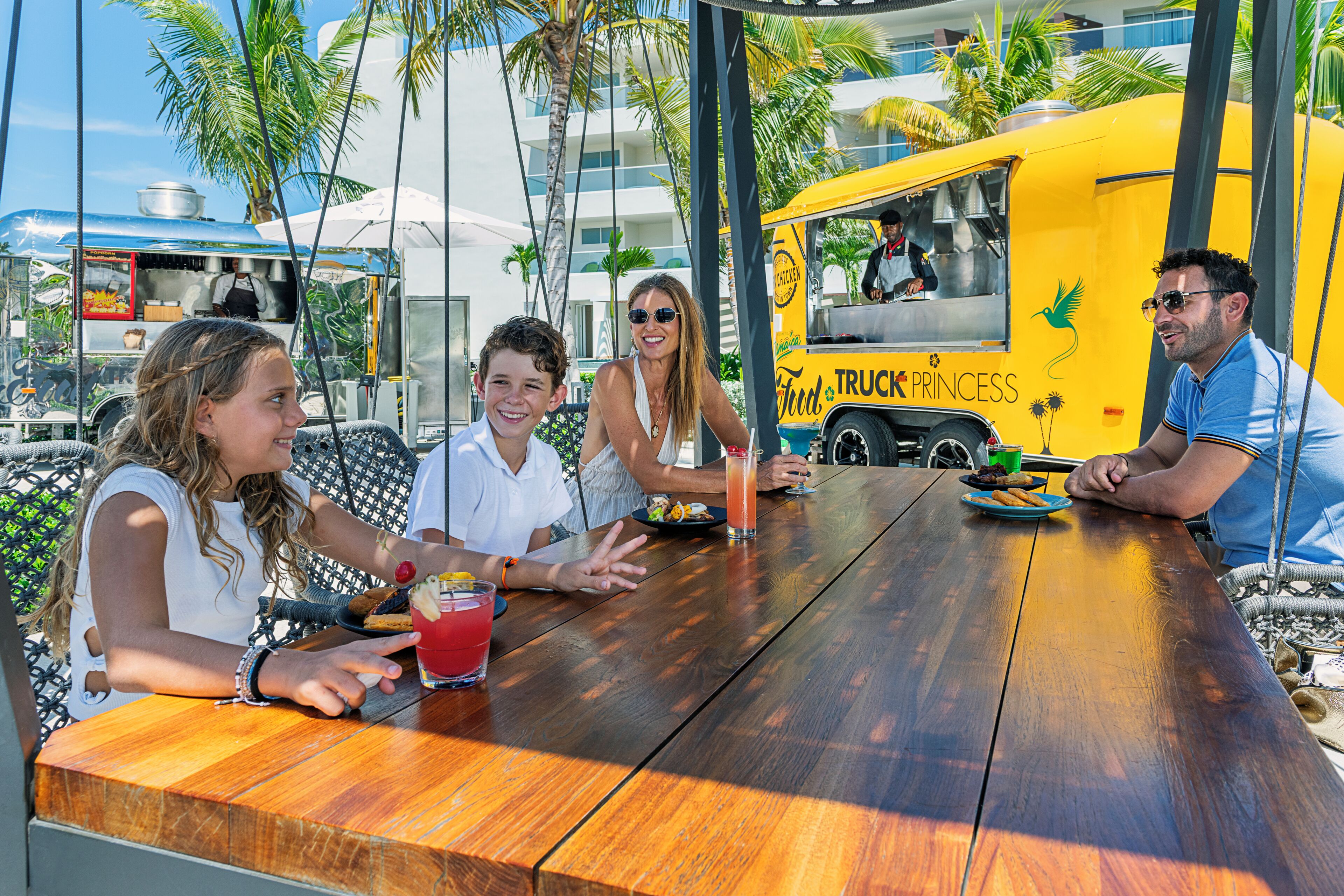 A group of people dining at an outdoor table with a food truck in the background.