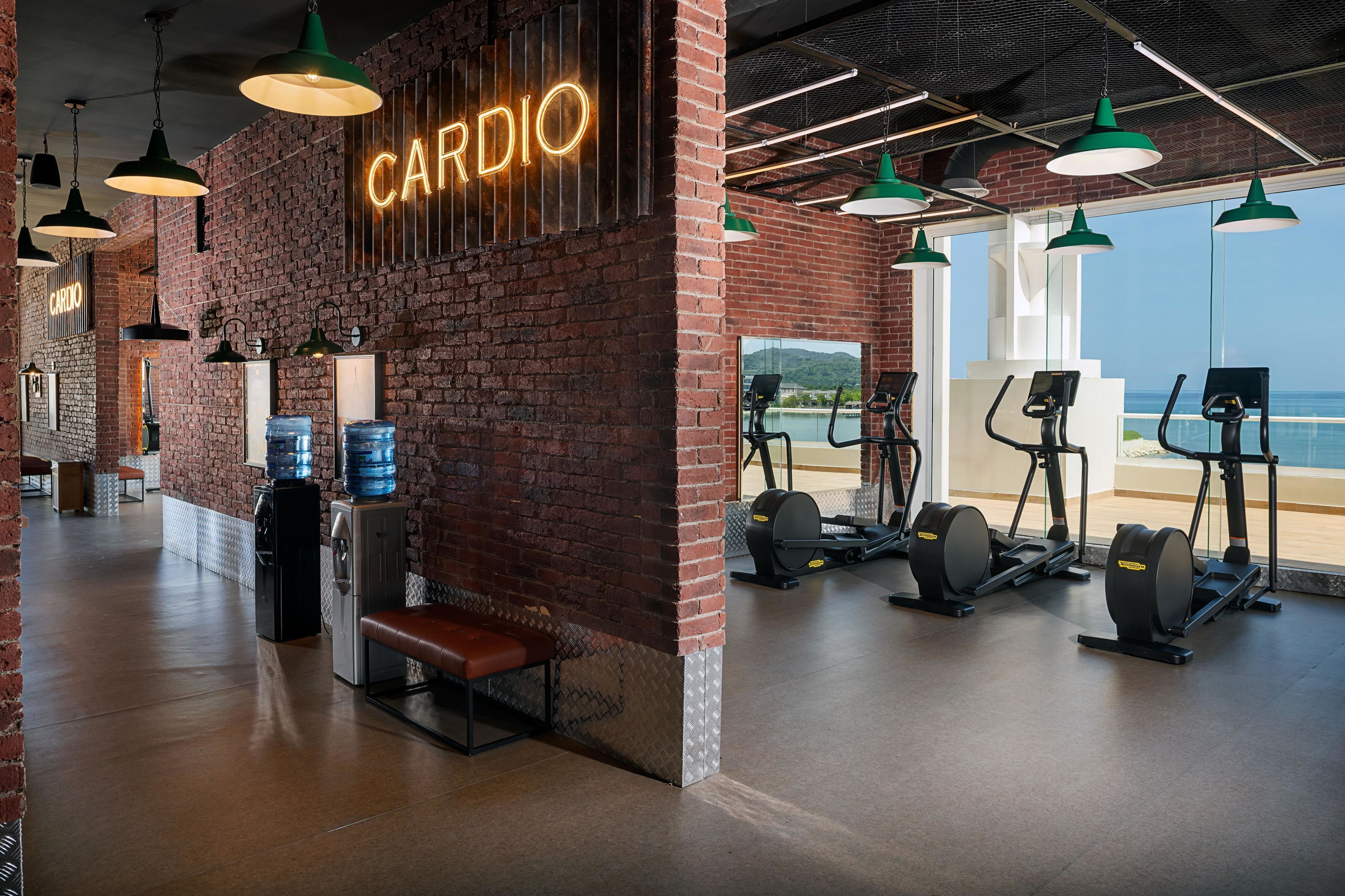 A gym with a brick wall, cardio equipment, and a bench.