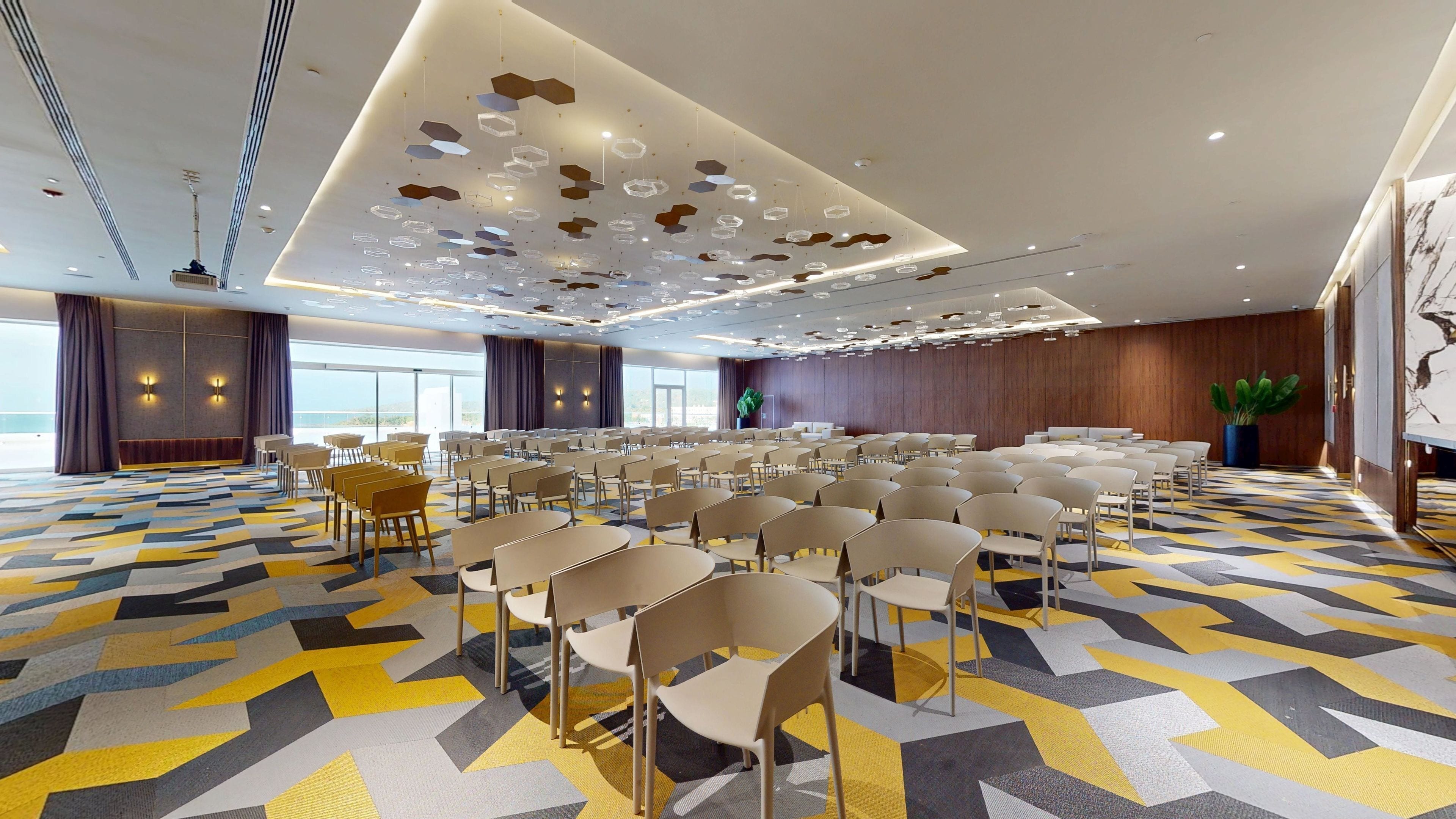 A conference room with rows of chairs, a patterned carpet, and a ceiling with geometric light fixtures.