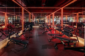 Ein Fitnessstudio mit verschiedenen Trainingsgeräten, darunter Bänke, Kurzhanteln und Kraftgeräte.