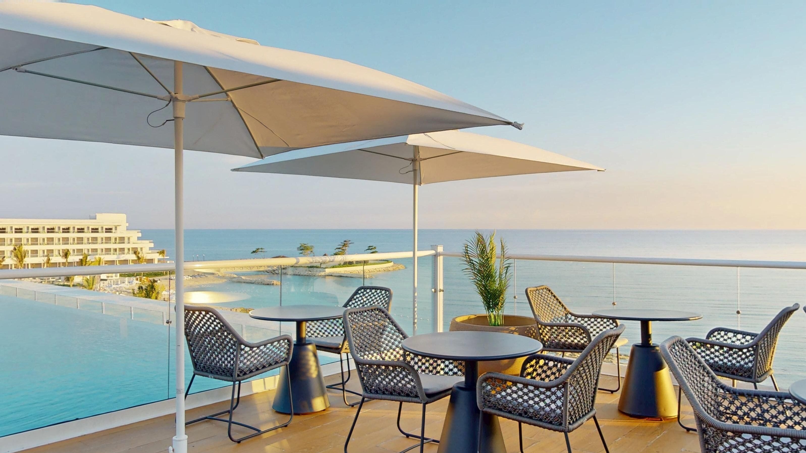 Terraza en la azotea con mobiliario exterior, piscina y vistas al océano y un edificio de resort.