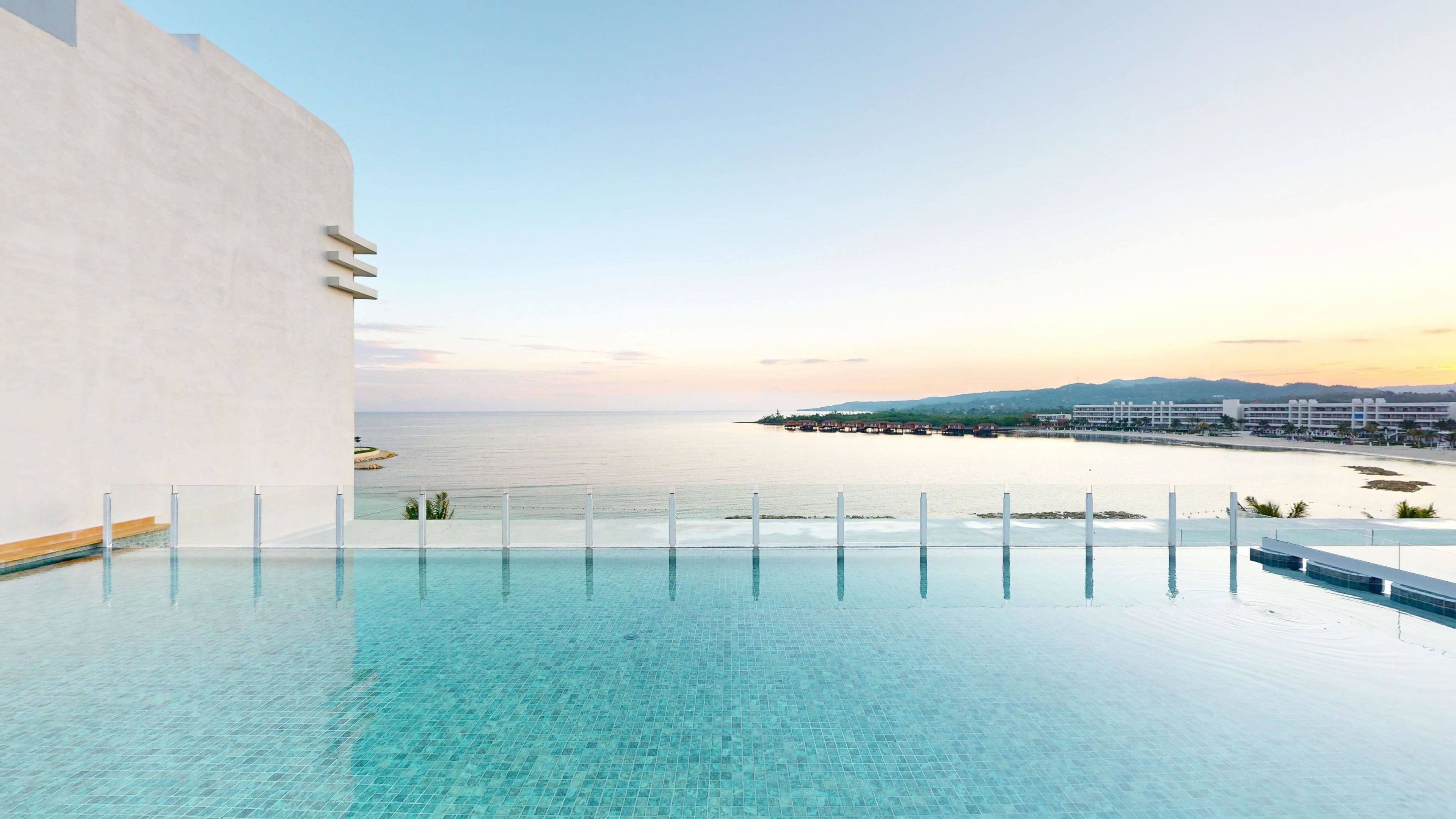 A rooftop infinity pool with a clear view of the ocean and a distant shoreline.
