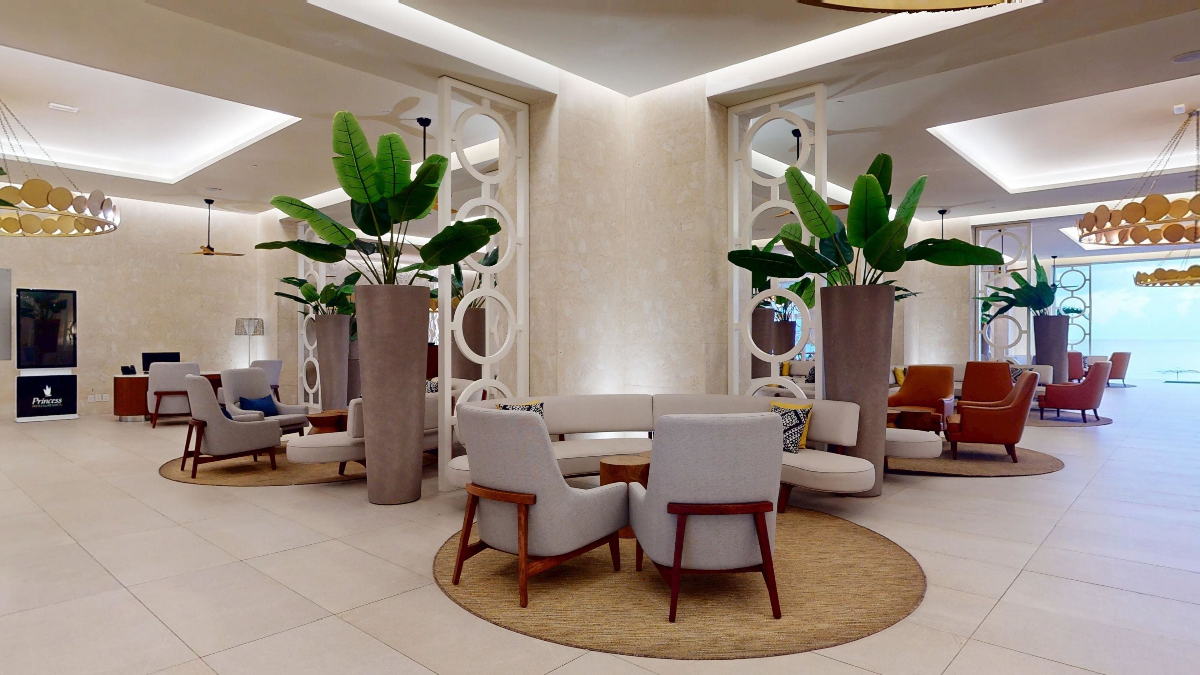 Un hall d’entrée spacieux, doté de meubles modernes, de grands pots de plantes et d’un plafond haut orné de lucarnes.