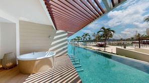 Un área de piscina moderna al aire libre con jacuzzi, agua azul cristalina y vistas a la playa y palmeras.