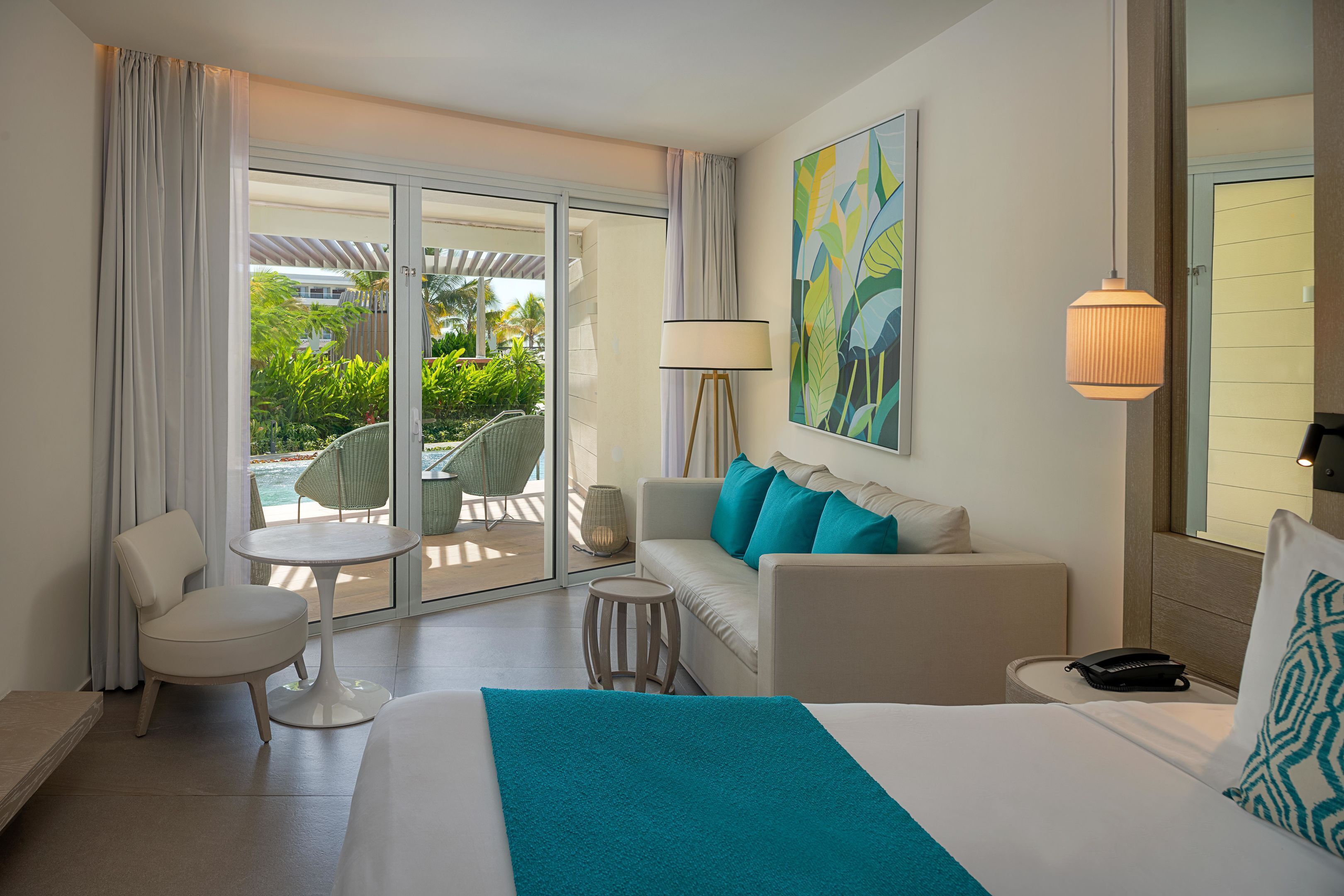 Una habitación de hotel con una cama, un sofá, una silla, una mesita, una lámpara y un cuadro en la pared.
