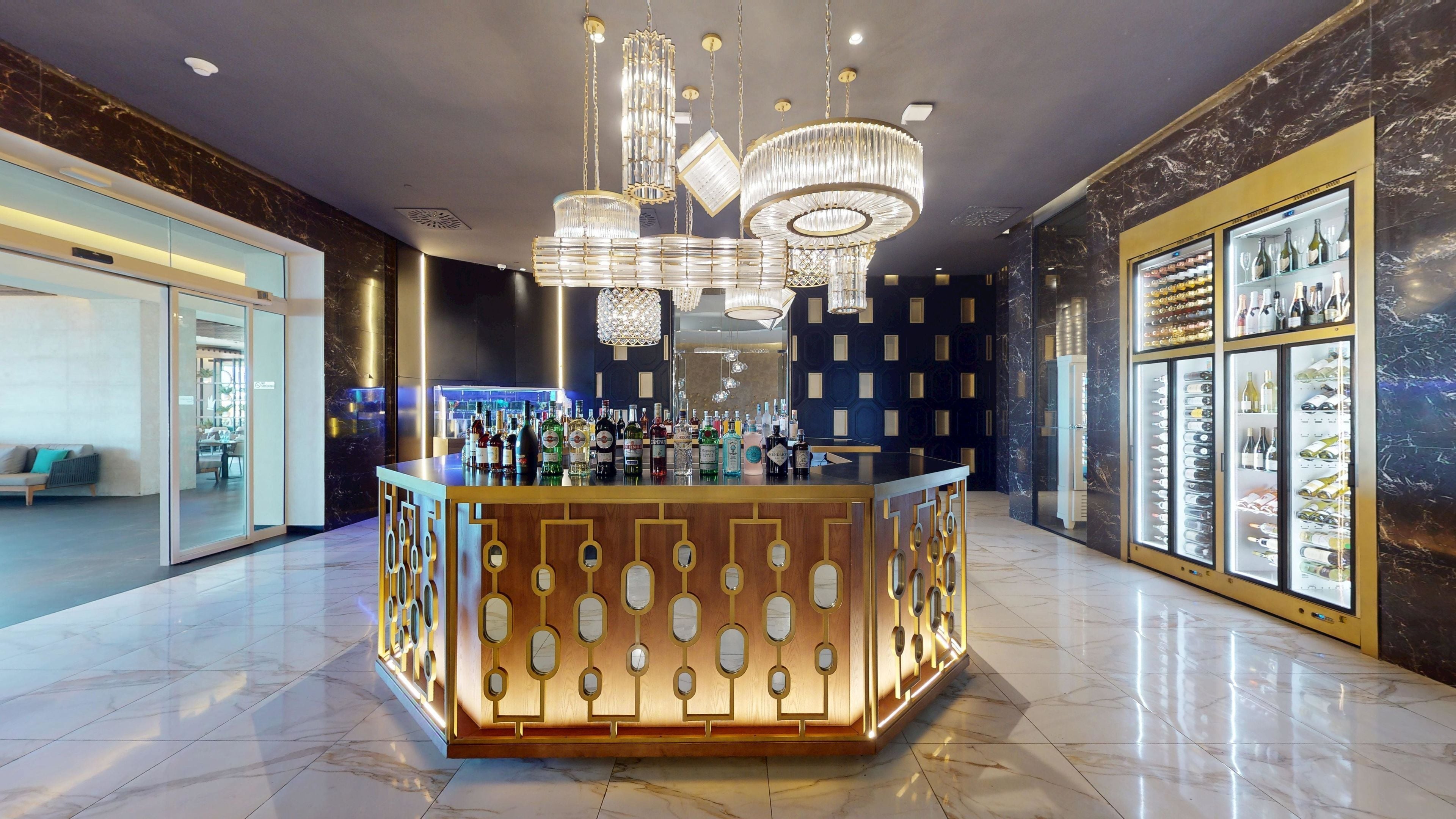 Angolo bar con pavimento in marmo, bancone dal design geometrico originale e parete ricca di bottiglie di vino.