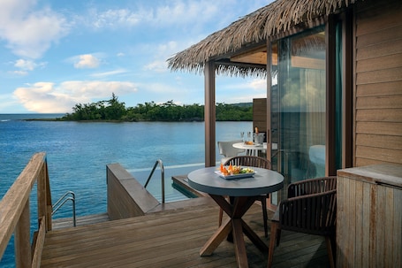 A wooden deck with a table and chairs, overlooking a body of water and a distant island.
