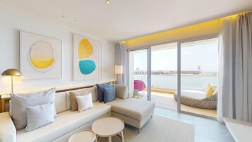 Habitación de hotel moderna con sofá, dos mesitas y vista al mar a través de amplias ventanas.