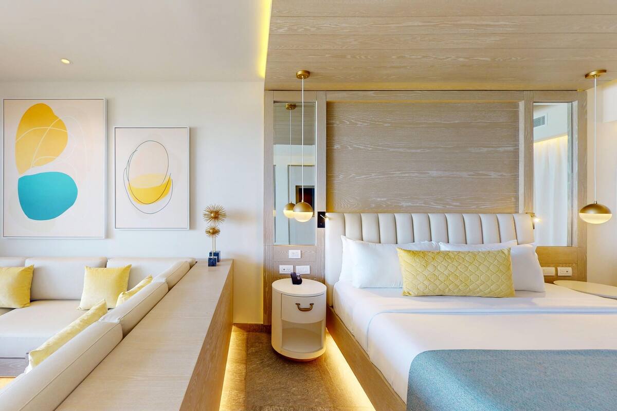 A modern hotel room with a sofa, a bed, a bedside table, and artwork on the walls.