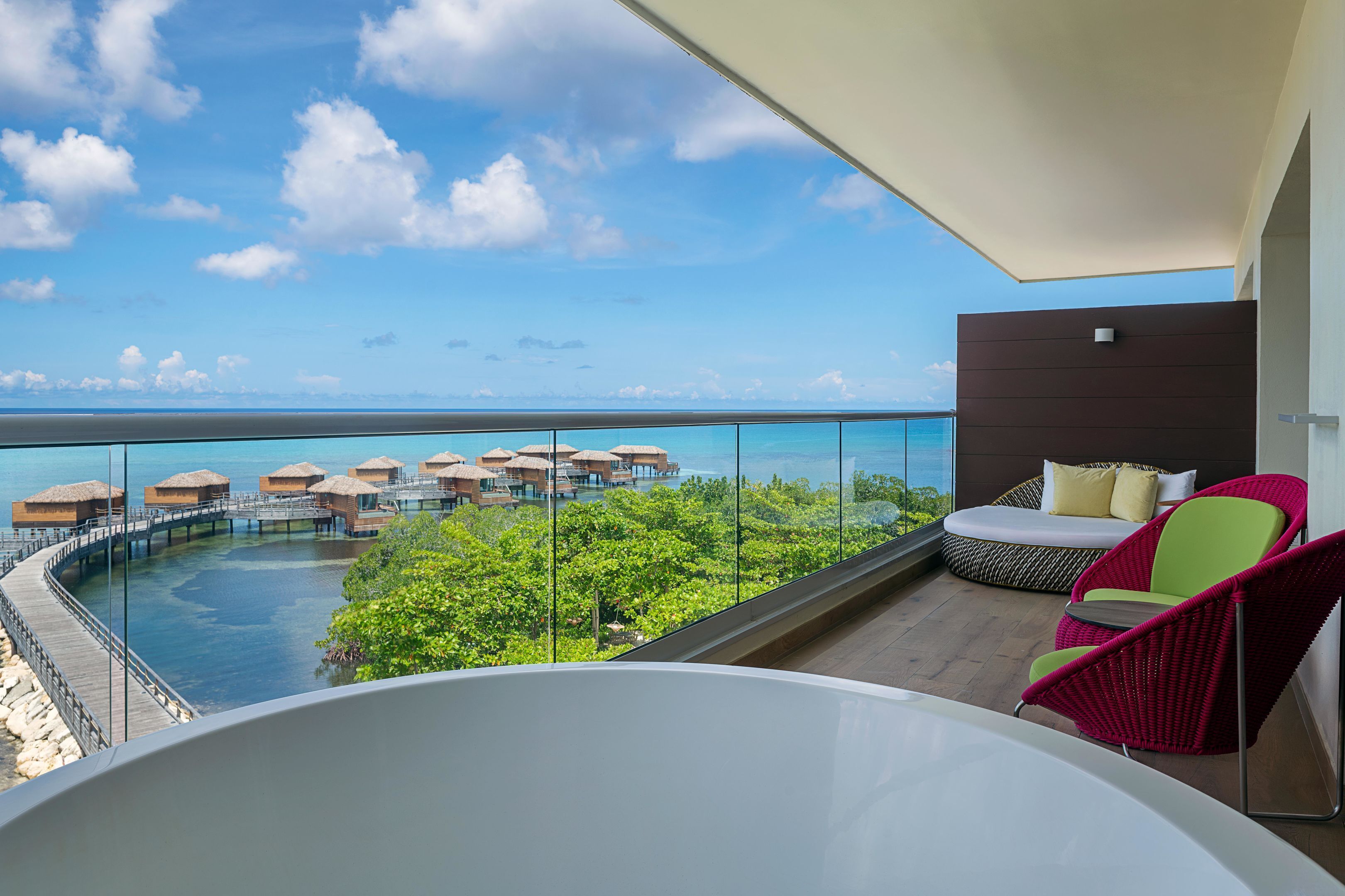 Un balcon offrant une vue sur les bungalows sur pilotis, une terrasse en bois et un espace salon avec des fauteuils.