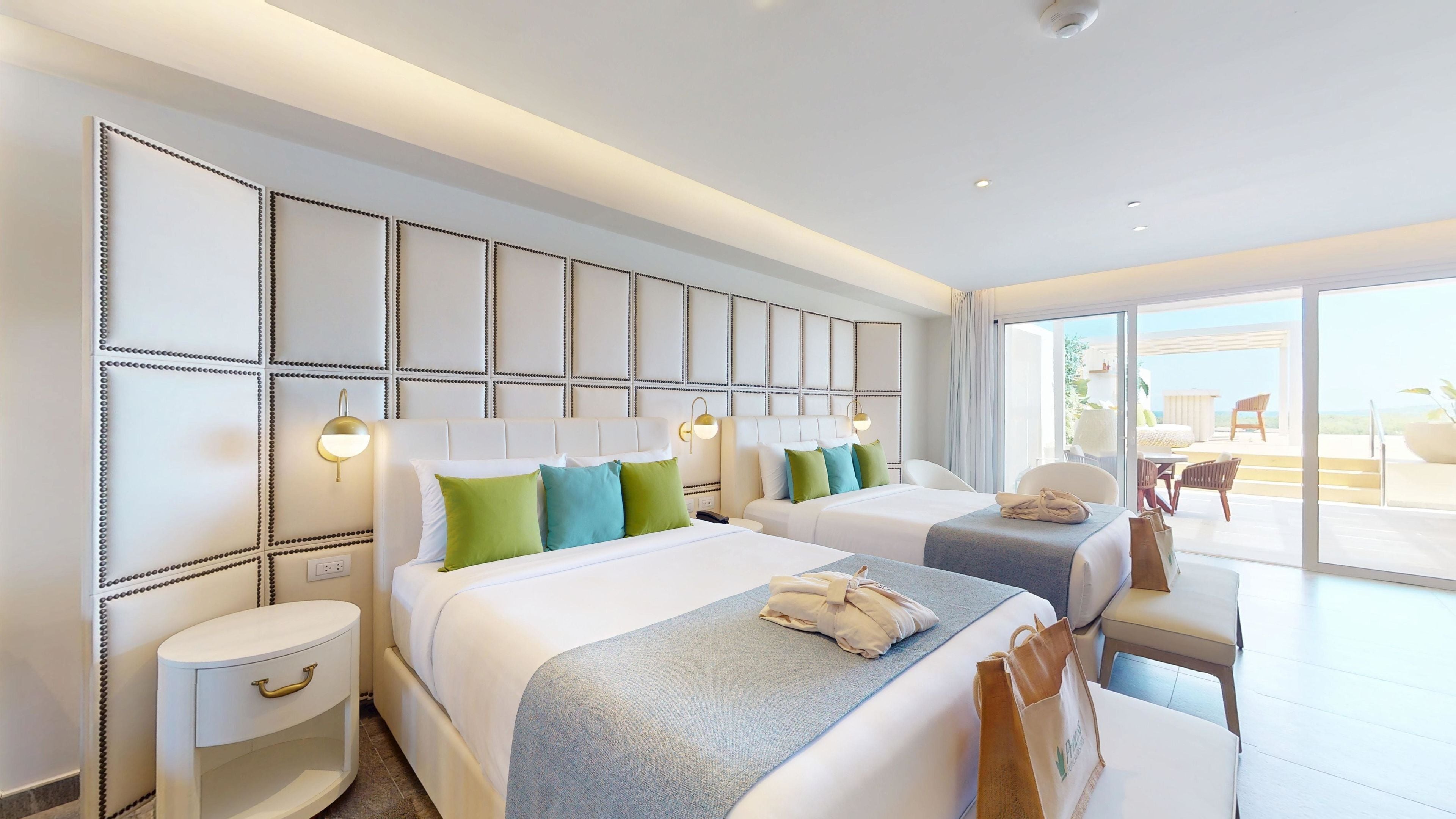 A hotel room with two beds, a sitting area with a table and chairs, and a balcony with a view.