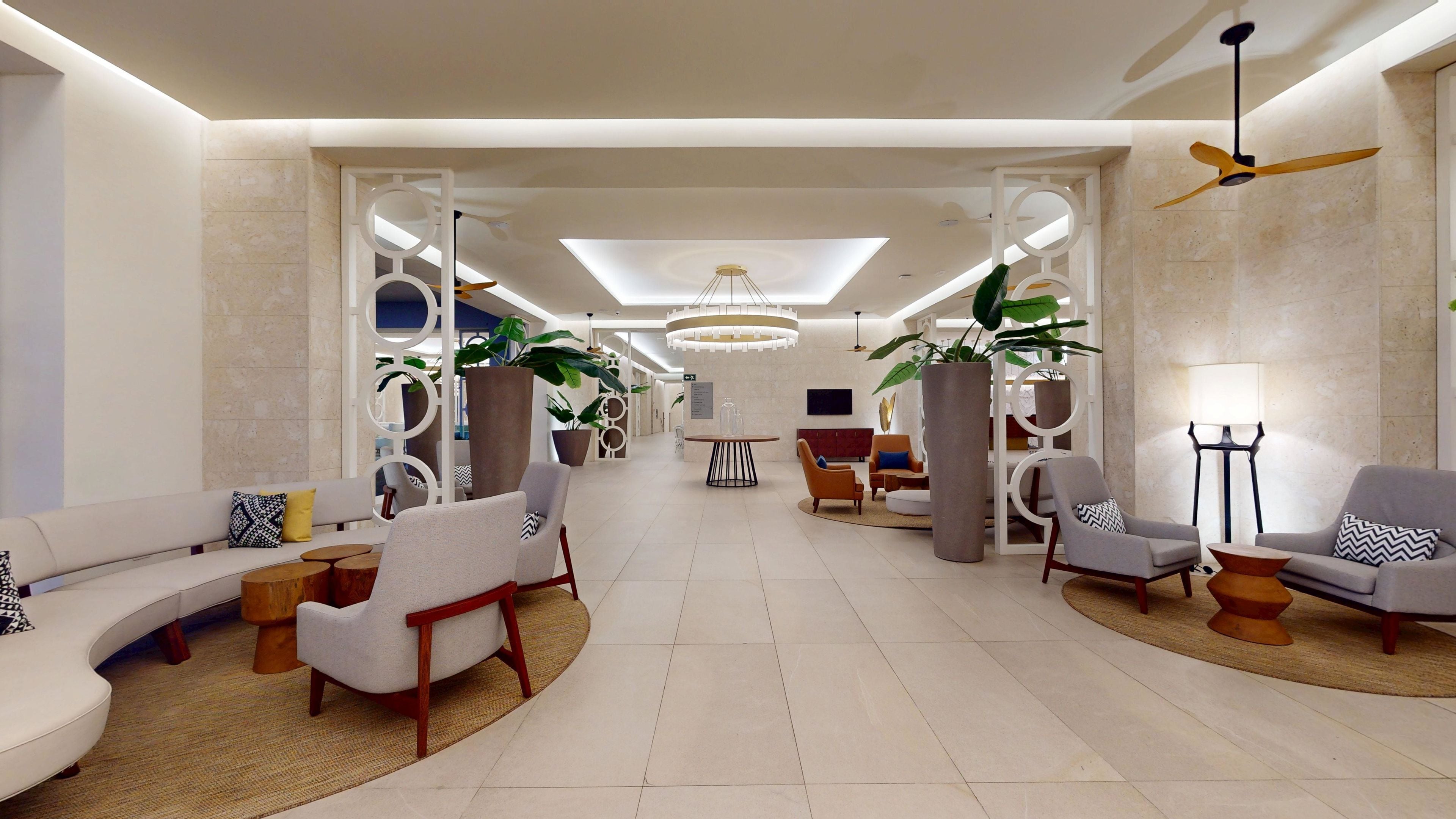 Un hall d’entrée spacieux, avec un canapé incurvé, des fauteuils, une table ronde et une grande plante en pot.