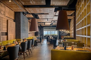 A restaurant with high ceilings, exposed brick walls, and pendant lighting. Tables are set with wine glasses and cutlery.