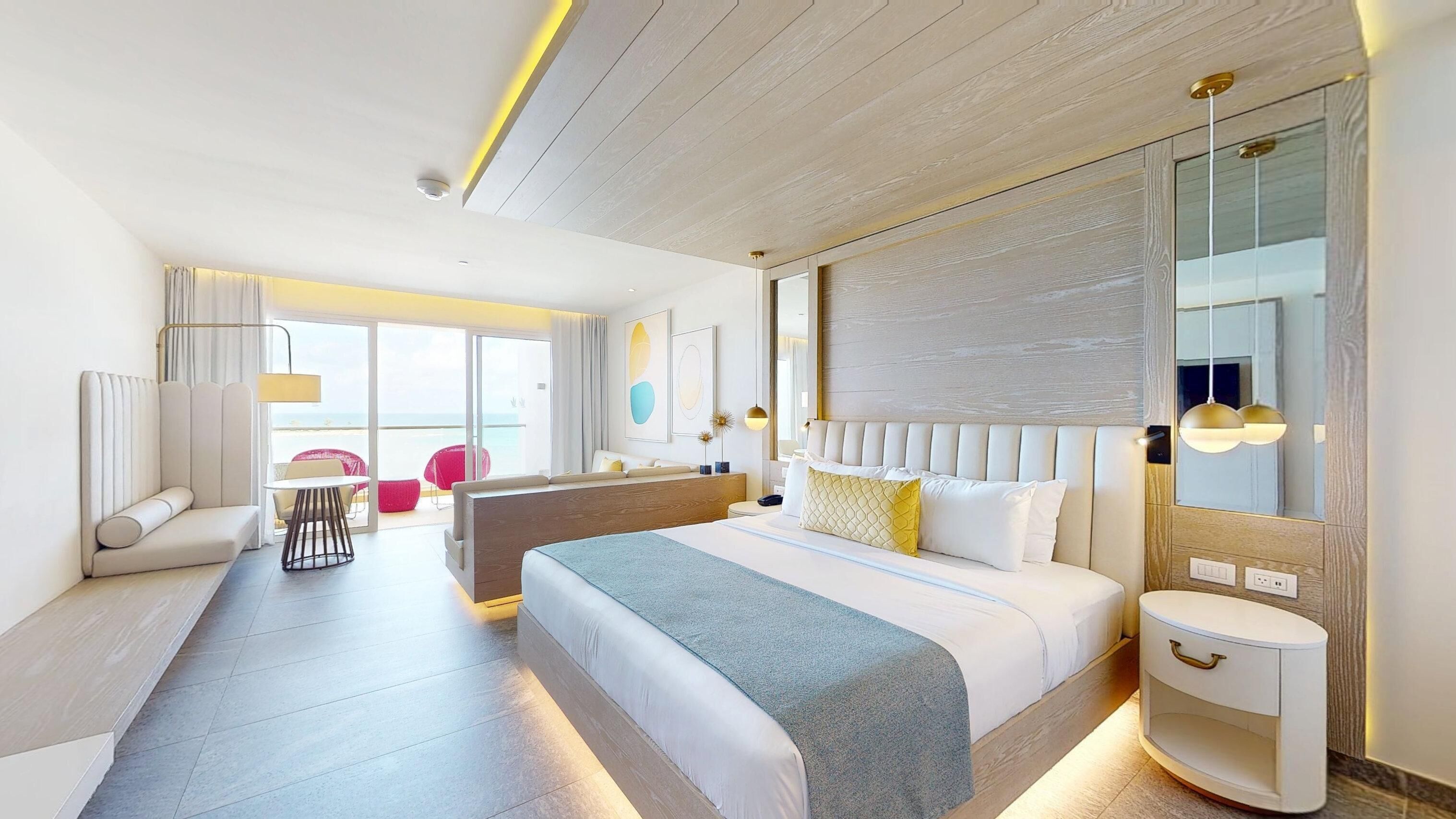 Una moderna camera d'albergo con un letto grande, un'area salotto con divano e poltrone, un tavolino e vista sul mare attraverso le porte scorrevoli in vetro.