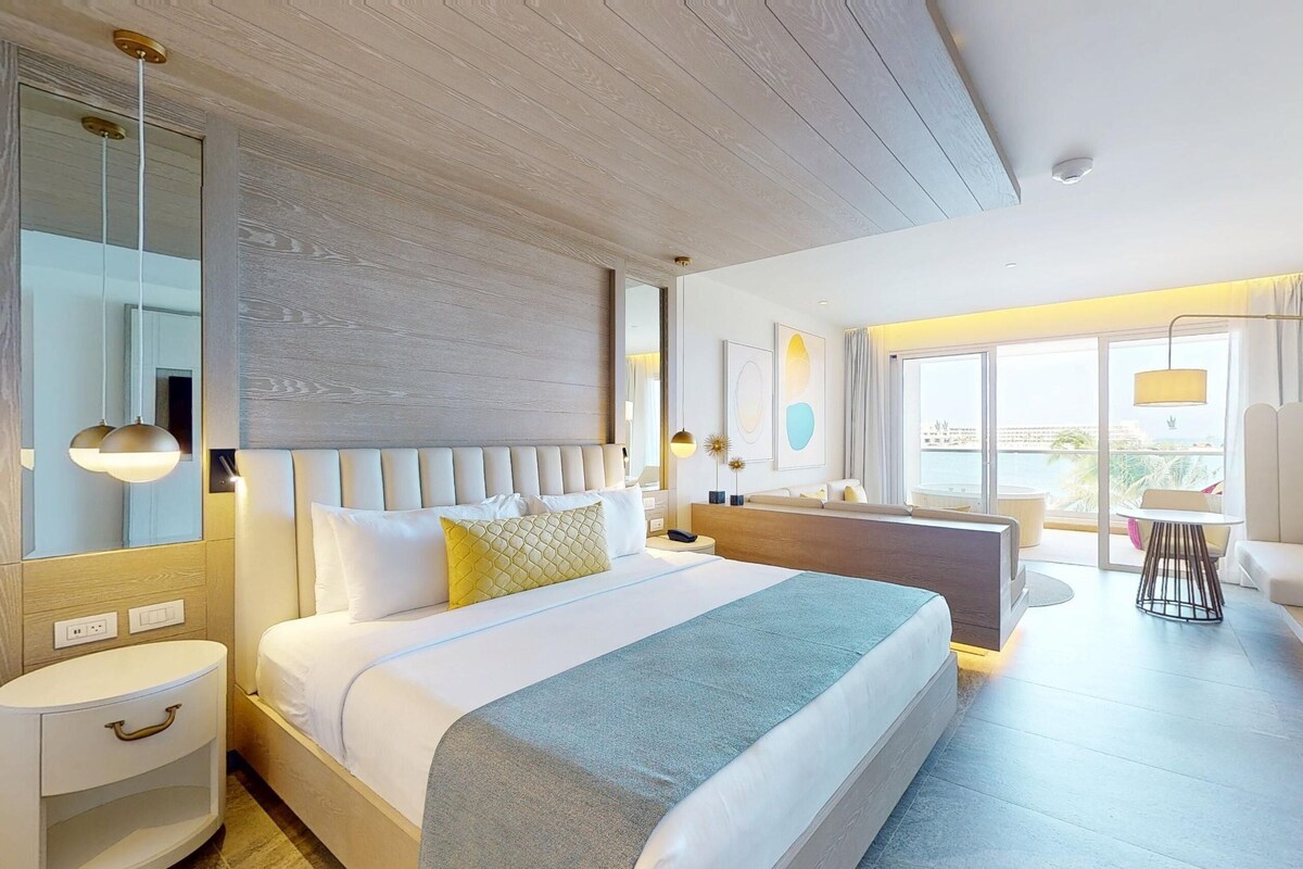 A modern hotel room with a large bed, a desk, a chair, and a view of the city.