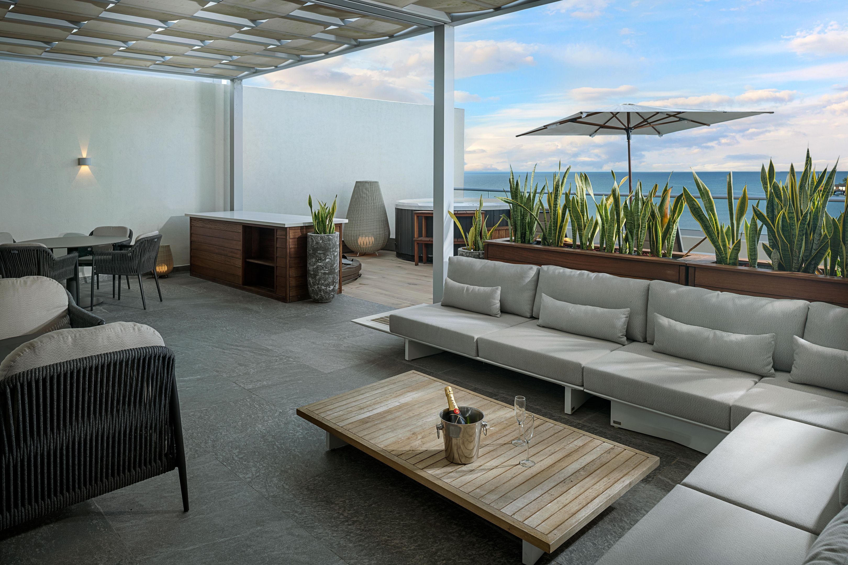 A modern outdoor seating area with a sofa, chairs, a coffee table, and a bar area.