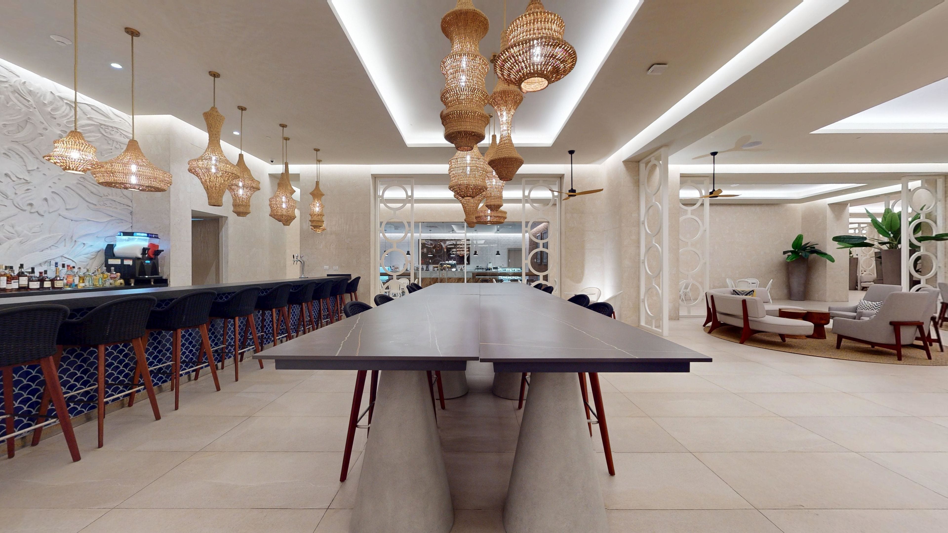 Un hall d’hôtel moderne avec une longue table à manger, un bar et un espace salon.