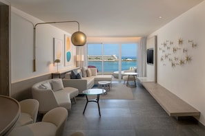 A modern hotel room with a large window, a sofa set, a glass coffee table, and a bench along the wall.