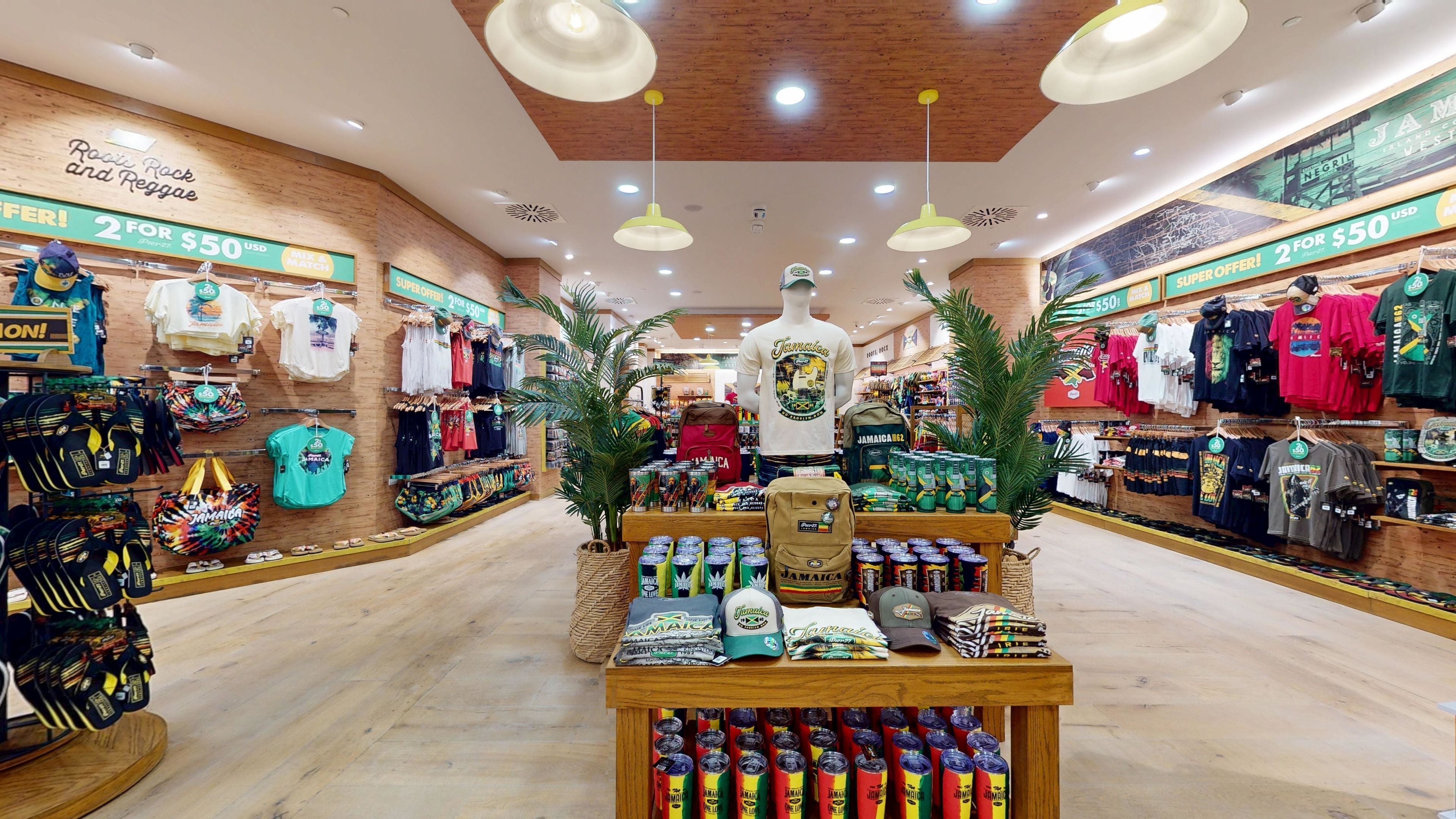 Interior de una tienda con suelos de madera, luces en el techo y un escaparate central con camisetas, gorras y bolsos.