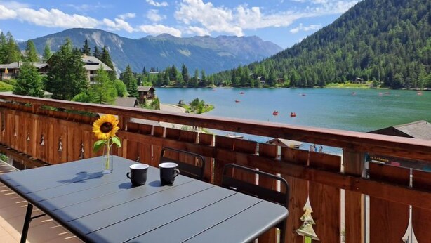 A wooden deck with a table and chairs, overlooking a lake with boats and mountains in the background. - Les Mayens 3.2 by Interhome (Champex)