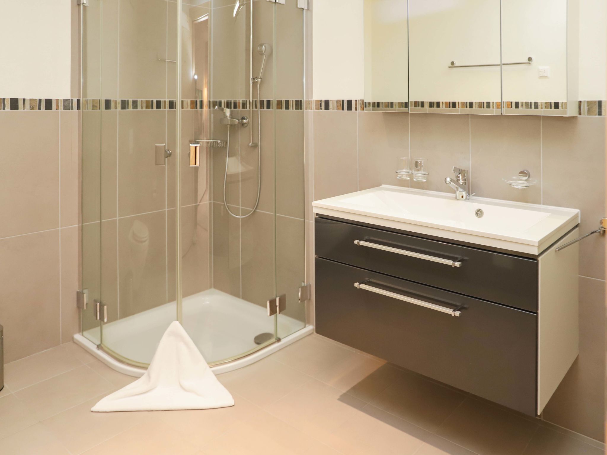 A modern bathroom with a glass shower enclosure, a white sink, and a dark vanity with drawers.