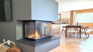 A modern living room with a fireplace, a dining area with a wooden table and chairs, and a kitchen in the background. - Les Mayens 3.2 by Interhome (Champex)