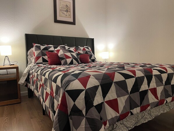 Una cama bien hecha con una colcha de estampado geométrico, dos lámparas de noche y un cuadro en la pared.