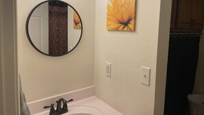 A bathroom with a round mirror, a sink, and a wall-mounted light fixture. - Vacation Condo #2 2BR with full kitchen, walk to river and shops, pets welcome (Hardy)
