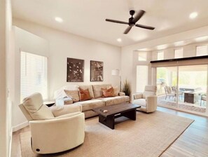 A spacious living room with a sofa, armchairs, a coffee table, and a ceiling fan.