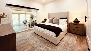 A modern bedroom with a large bed, a nightstand, a desk, and a sliding glass door leading to a balcony. - Sun & Fun in Fountain Hills- HENDVR2 (Fountain Hills)