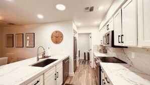 A modern kitchen with white cabinetry, a marble countertop, and a wooden floor. - Sun & Fun in Fountain Hills- HENDVR2 (Fountain Hills)